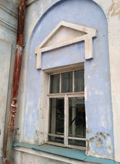 The old arc window with the wooden frame and the white-blue exfoliated stone wall