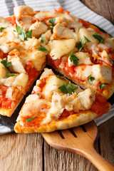 sliced buffalo pizza with chicken, tomatoes, greens and mozzarella close-up on the table. vertical