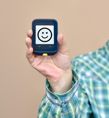 Hand of a person holding and showing glucose meter. The monitor shows SMILEY face. Selective focus. 