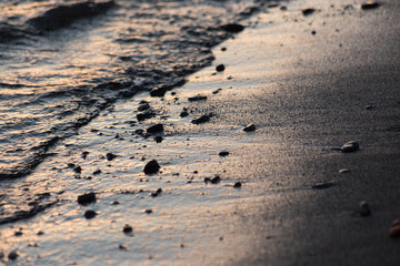 A close view of water on a lake shore at sunset, with details of sands and little round stones