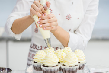 Close up hands of the chef with confectionery bag squeezing  cream on cupcakes