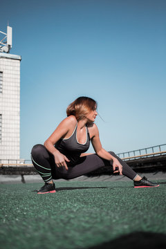Young sportive woman doing deep lunges on the roof. Beautiful girl doing workout oudoors.