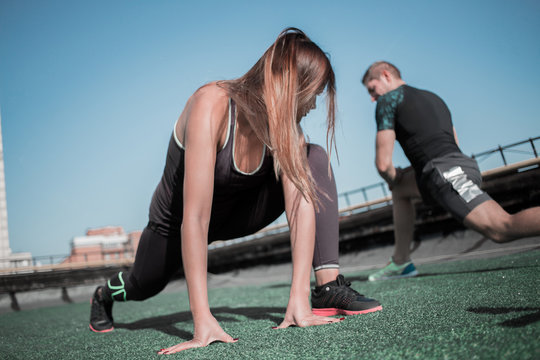 Sportive man and woman doing lunges outdoors. Young people training on the roof of the building.