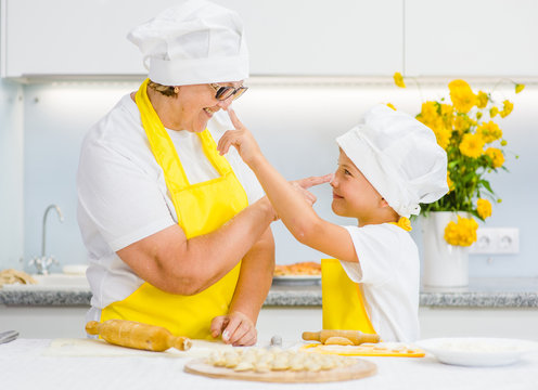 Senior woman and young boy indulge in the kitchen, trying to stain each other with flour