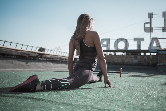 Sport on the roof, female stretching out on green carpet. Sportive woman sitting in cross twine.