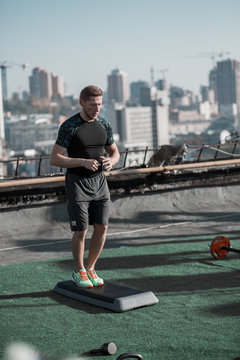 Young athletic man getting ready for workout on the roof. Sport exercises on the roof with nice city view.