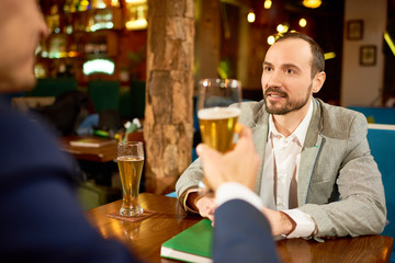 Two smiling business partners having informal meeting in pub: they drinking beer and discussing details of mutually beneficial cooperation