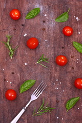 Fresh tomatoes, rosemary, basil and spices on a wooden table.