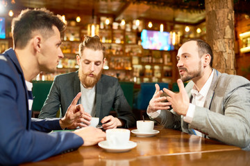Group of talented managers gathered together in modern cafe, drinking fragrant coffee and sharing ideas with each other concerning start-up project