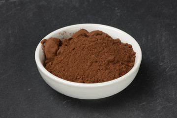 Cacao en polvo en un bol de cerámica blanco sobre un fondo de piedra negra