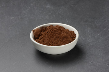 Cacao en polvo en un bol de cerámica blanco sobre un fondo de piedra negra