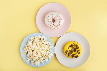 donuts and popcorn on multi-colored plates on a yellow background, close-up, top view