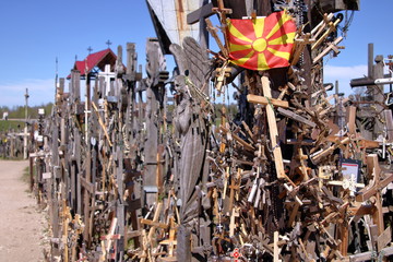Krzyże drewniane, metalowe, żeliwne na Górze Krzyży, Litwa, pomiędzy krzyżami flaga Macedonii, słonecznie - obrazy, fototapety, plakaty
