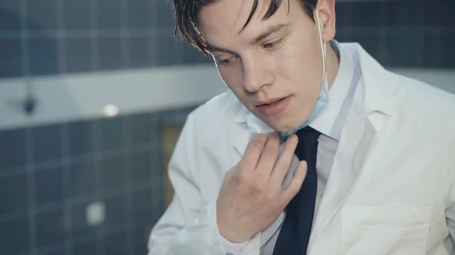 Tired young doctor undressing uniform after operation