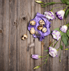Easter quail eggs with eustoma flowers  and purple craft paper on rustic wooden background. Holiday art design background. Easter.