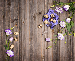 Easter quail eggs with eustoma flowers  and purple craft paper on rustic wooden background. Holiday art design background. Easter.