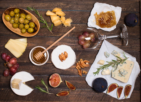 Cheese selection on wooden rustic board. Cheese platter with different cheeses, grapes, nuts, honey and figs on weathered wood background.