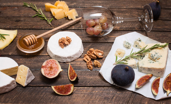 Cheese selection on wooden rustic board. Cheese platter with different cheeses, grapes, nuts, honey and figs on weathered wood background.