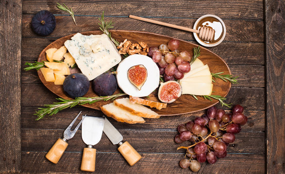 Cheese board. Various types of cheese. Cheese plate with cheeses Parmesan, Brie, Camembert and Roquefort  serving with grapes, honey, nuts, olives  and bread on wooden board.