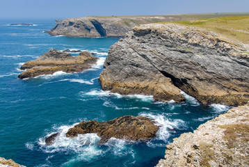 The sea is blue, the waves break on the rocks and the tormented cliffs on the wild coast of Belle-Ile, Brittany, France