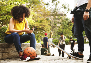 Young adult friends chilling at the park using smartphones and skateboarding youth culture concept