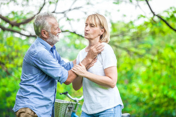 Fototapeta premium Elderly woman have chest pains or heart attack in the park with senior man, health care concept.