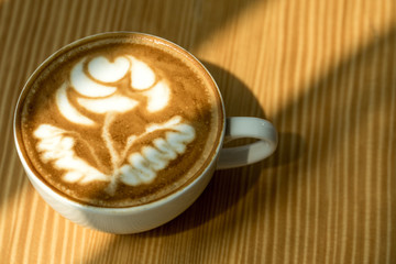 Hot Latte art coffee white cup on Wooden table and wood background texture wallpaper with nature sun light