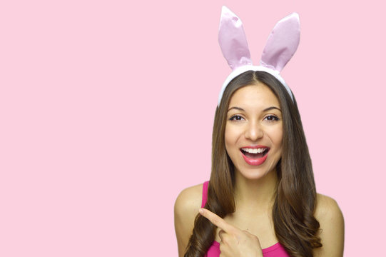 Attractive cheerful girl with bunny ears pointing your product or logo isolated on pink background. Copy space. Easter concept. 