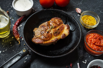Juicy pork steak with spices on pan on dark stone background