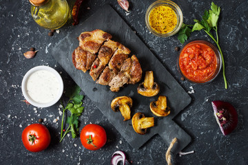 Juicy pork steak with spices and grilled mushroomson dark stone background. Top