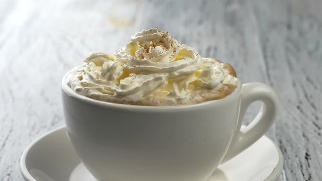 Cinnamon powder sprinkling on whipped cream in cappuccino coffee cup. Slow motion shot.
