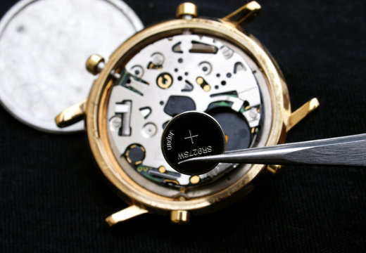 watchmaker change battery, close up of battery and quartz watch caliber in the background