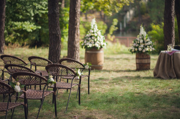 Decorations for a wedding ceremony in nature. Wooden chairs, wedding arch, table with flowers, glasses and rings.