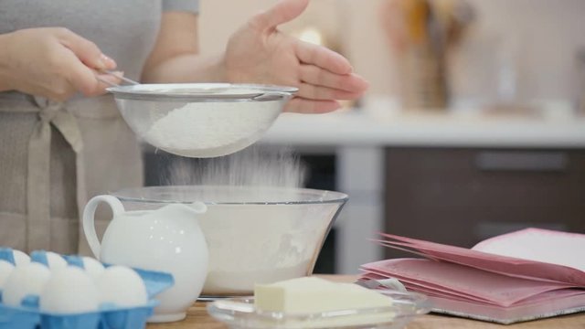 Cinemagraph - Woman  sifting flour through a sieve for baking and on the table lies a recipe book . Motion Photo.
