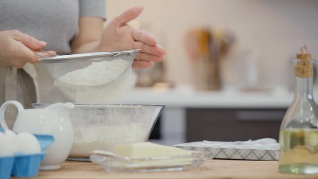 Cinemagraph - Woman  sifting flour through a sieve for baking and on the table lies a recipe book . Motion Photo.