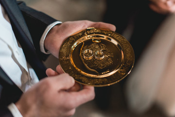 golden wedding rings on a golden plate in the hands of a witness in the church