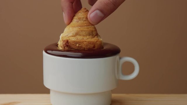 closeup of croissant immerse into hot chocolate in cup. Hot chocolate take out of cup making smuges