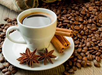 Coffee beans and coffee cup with cinnamon and anise on wooden board