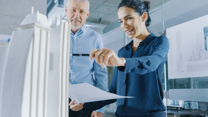 Two Professional Male and Female Architectural Engineers Work with Blueprints and on a Building Model Design for the Urban Planning Project.