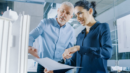 Obraz premium Two Professional Male and Female Architectural Engineers Work with Blueprints and on a Building Model Design for the Urban Planning Project.