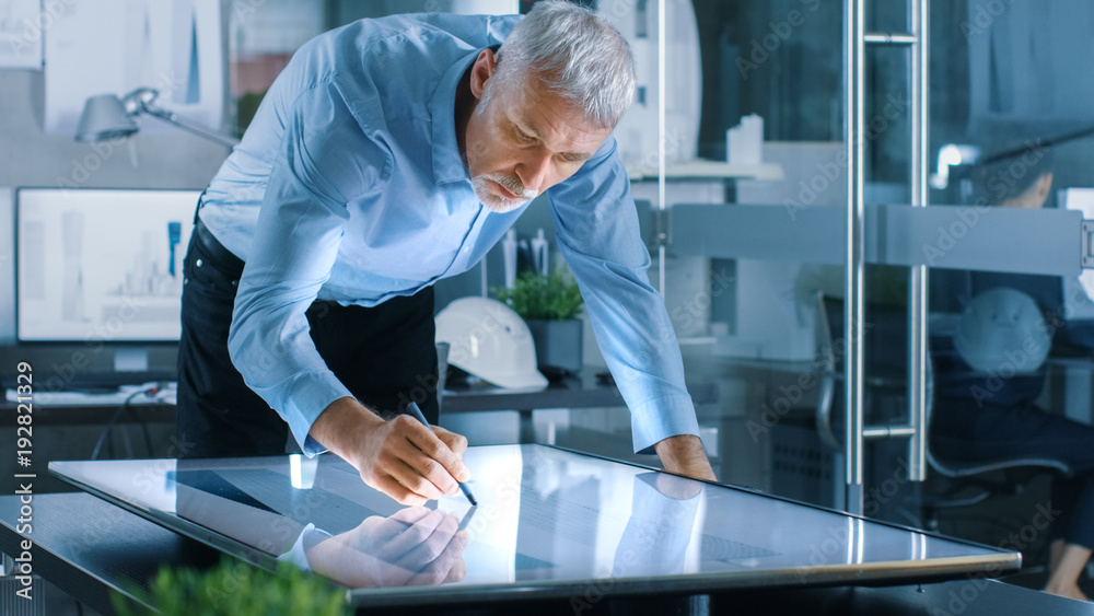 Aufkleber Senior Architectural Engineer Draws Building Concept on a Graphics Tablet Display Vertical Touchscreen Table. Clean Minimalistic Office, Concrete Walls Covered by Blueprints.