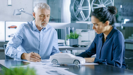 Obraz premium Experienced Automotive Designer and Female Engineer Works with Blueprints and Sketches of a New Car Prototype Model.