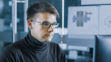 Obraz premium Young Male Industrial Engineer Works on a Personal Computer. Handsome Smart Man in the Bright Modern Office.