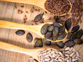 Flaxseed, pumpkin and sunflower seeds in wooden spoons.