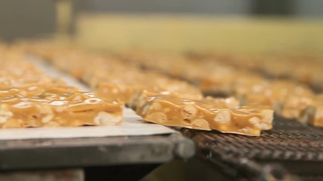 Nougat with peanuts close-up. Cutting a long line of viscous nougat into bars. Bars of nougat with peanuts on the production line of the factory for the production of sweets.