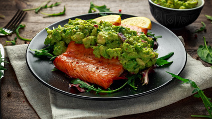 Oven cooked salmon steak, fillet with avocado salsa and green on black plate. wooden table. healthy food