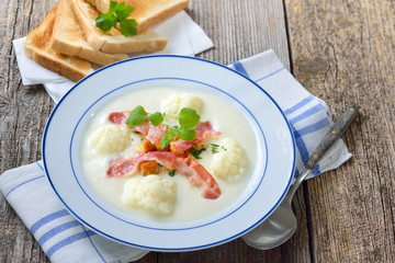 Delikate Blumenkohl-Cremesuppe  mit gebratenen Speckstreifen und Croutons, serviert mit knusprigem Weizentoast – Cauliflower cream soup topped with fried bacon and croutons, served with crisp toast