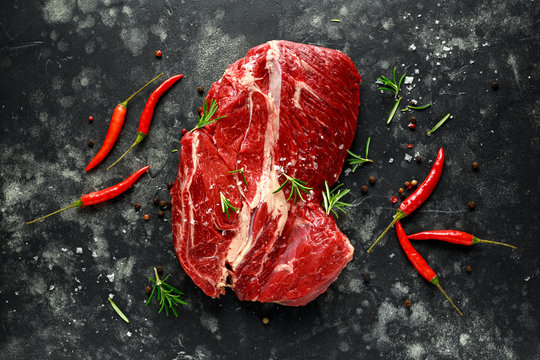 Fresh Raw braising steak on black background with rosemary, chilli, pepper