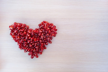 Heart made from grains of garnet on wooden table. Space for text