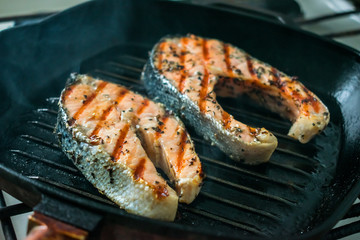 Two two toasted salmon steaks with spices and herbs on a grill pan. Close up bbq grilled salmon steaks on black cast-iron ribbed frying pan. Healthy, fitness food, diet. Selective focus